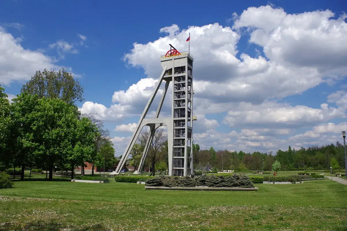 Betonowy szyb górniczy, dawniej symbol przemysłu, dziś stanowi pomnik. Szyb Prezydent w parku, pod błękitnym niebem.