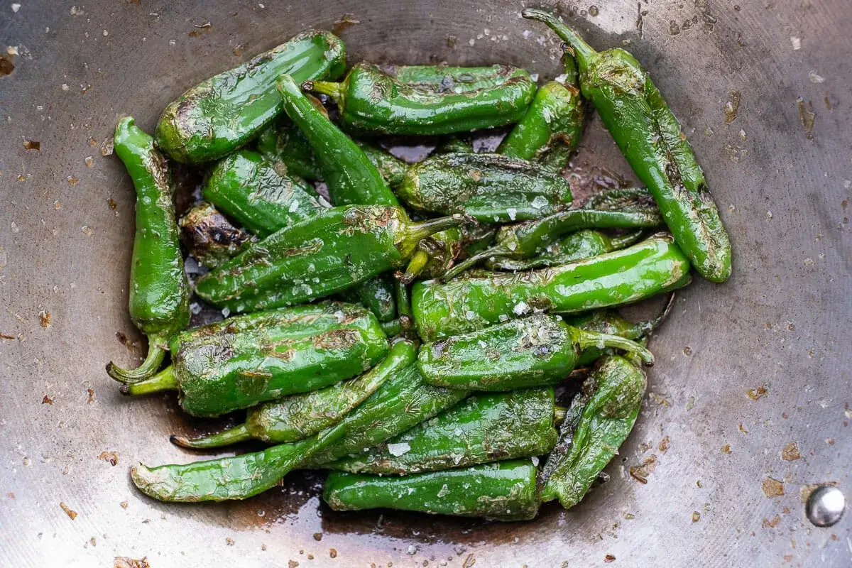 Gr&uuml;ne Paprika werden in einer Pfanne zubereitet, leicht gebr&auml;unt und mit Salz bestreut.