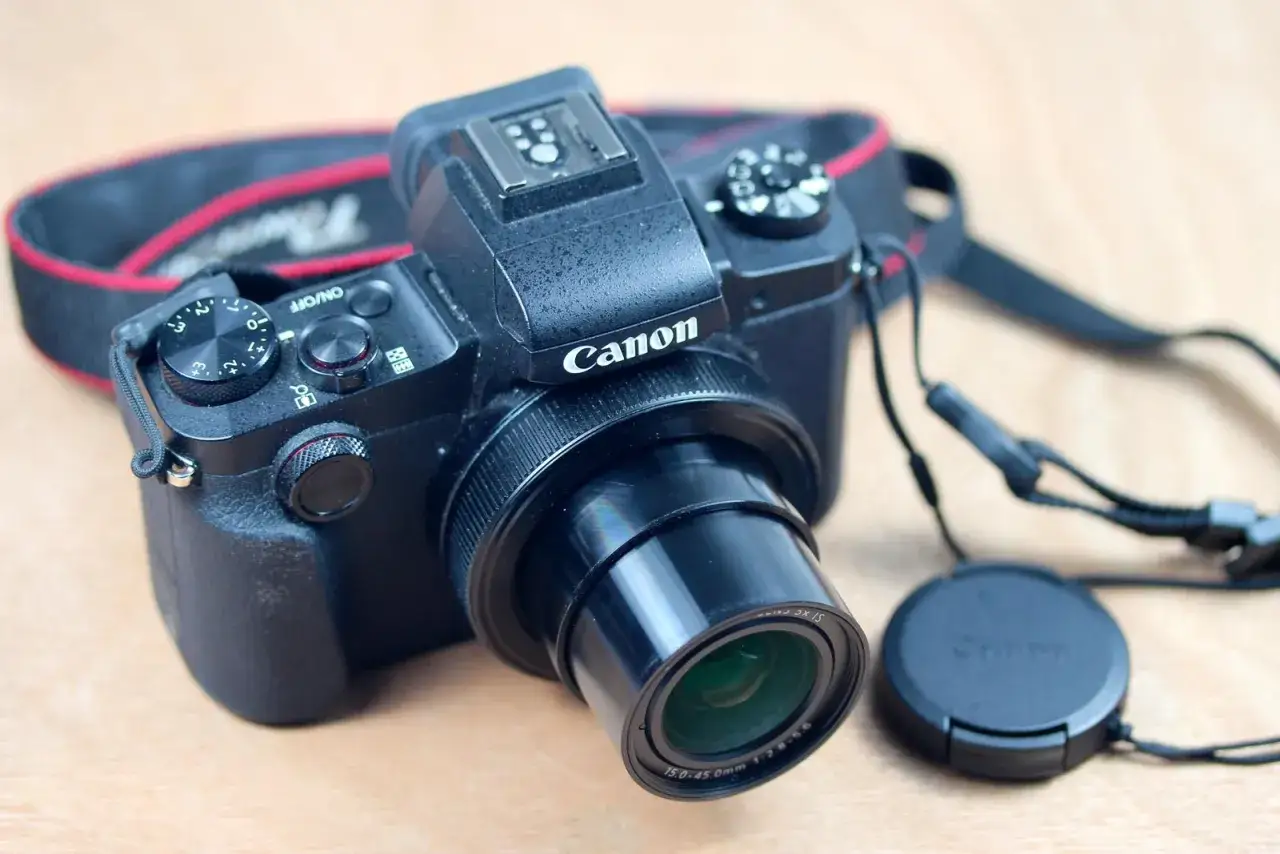 Un appareil photo noir Canon G1X Mark III, pr&ecirc;t pour un test. Son objectif est visible, avec sa sangle autour.