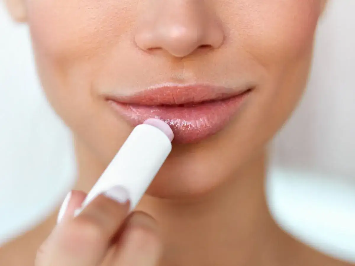 Frau tr&auml;gt Lippenbalsam auf, um trockene Lippen zu pflegen.