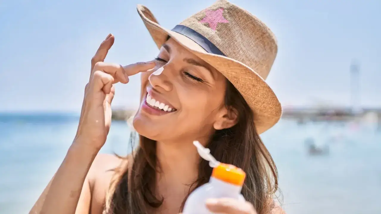 Mujer sonriente se aplica protector solar factor 50 en la nariz en la playa.