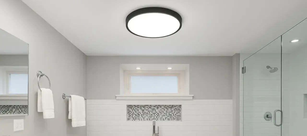 Salle de bain moderne avec plafonnier rond noir. Idéal pour changer ampoule plafonnier hublot. Douche vitrée, lavabo et serviettes blanches.