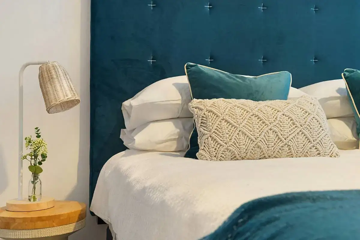 Cabecero tapizado en terciopelo azul, con cojines de macram&eacute; y terciopelo. Ideas para hacer un cabecero acogedor.