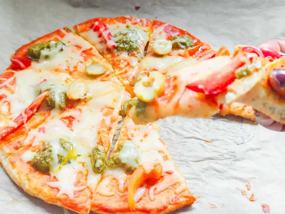 Pyszna pizza z serka wiejskiego, z zielonym pesto i pomidorami, właśnie jest podnoszona do jedzenia.
