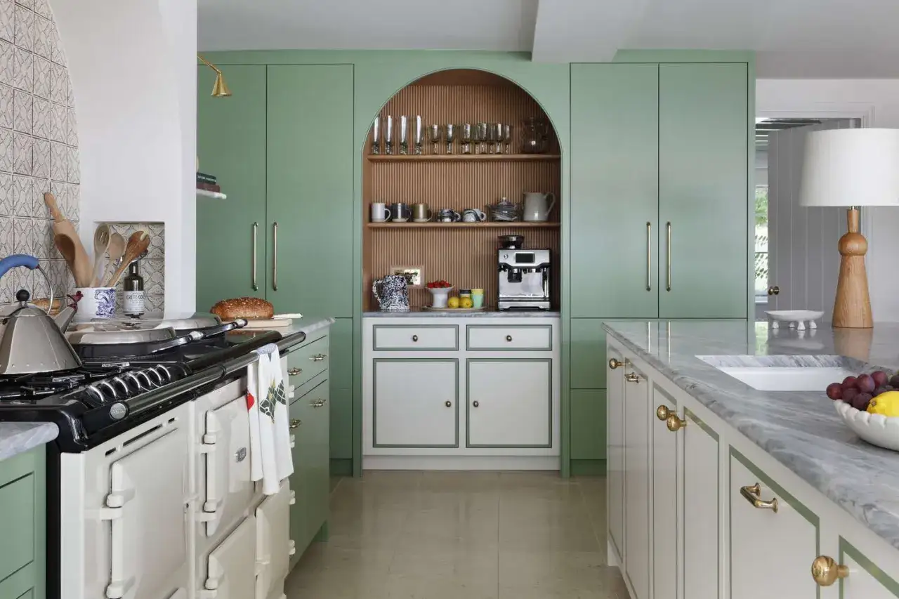 Cocinas verdes con encanto: armarios pastel, estantería arqueada con cristalería y cafetera, y una isla de mármol.
