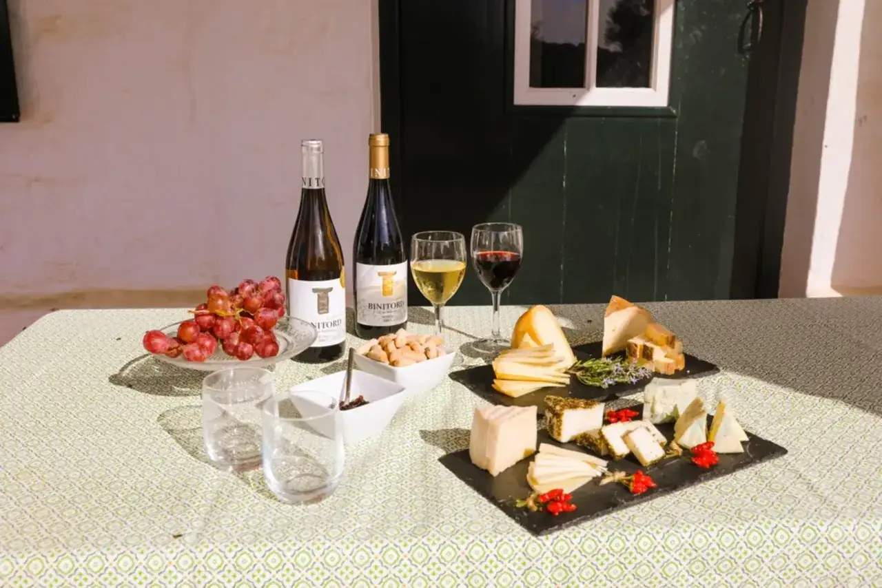 Degustaci&oacute;n de quesos y vinos en finca La Malcriada Dulce. Uvas, dos botellas de vino, copas, quesos variados y aperitivos sobre mantel verde.