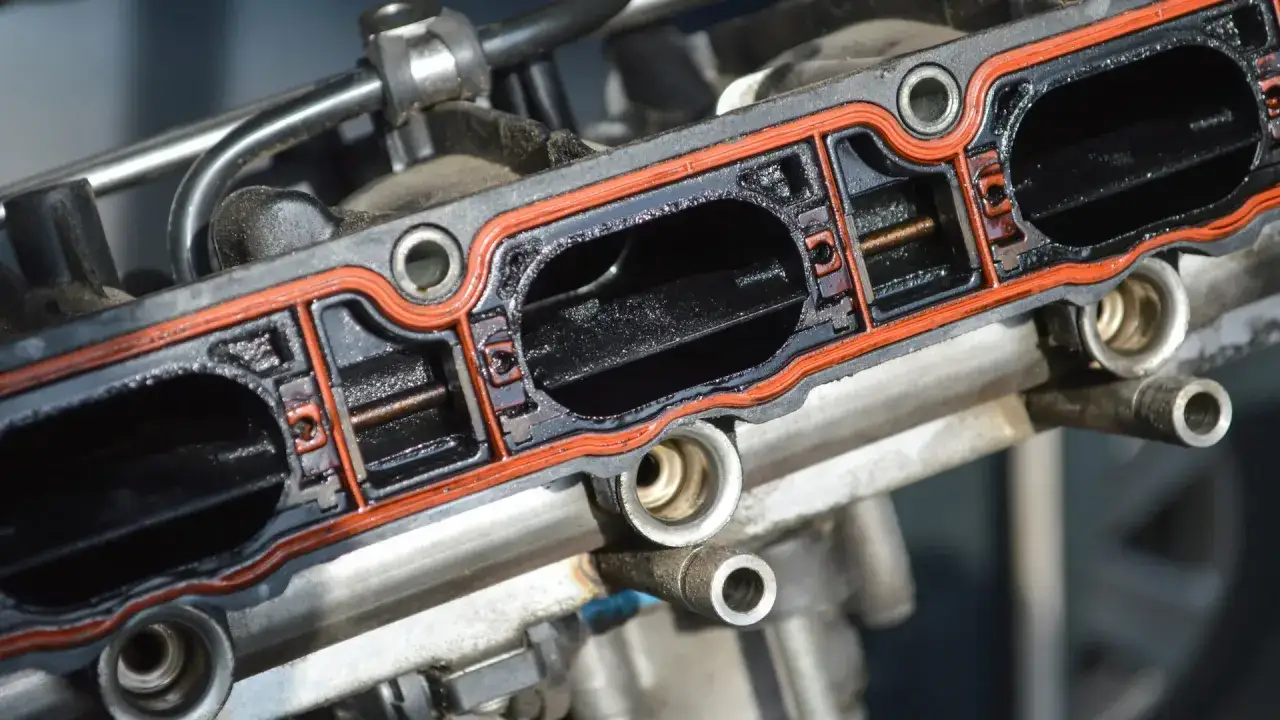 Close-up of a dirty intake manifold gasket, showing the orange seal and black carbon buildup within the intake runners.
