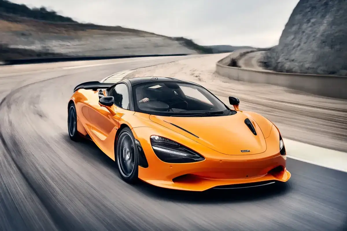 Pomarańczowy McLaren 750S z czarnym dachem śmiga po torze wyścigowym, zostawiając za sobą smugi.