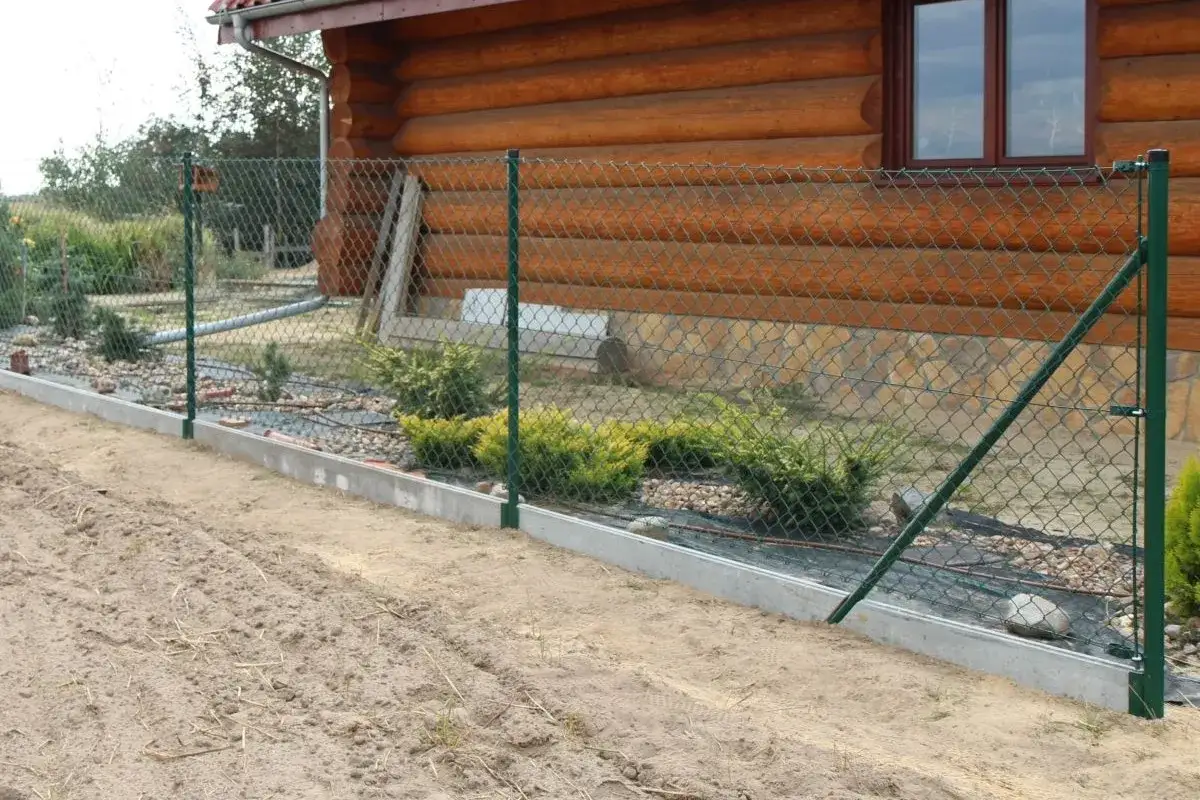 Zielone słupki do siatki 150 cm stabilizują ogrodzenie przy drewnianym domu.