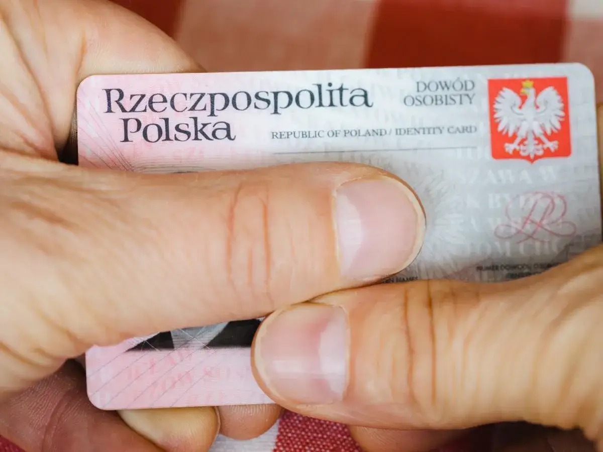 Dłonie trzymają dowód osobisty Rzeczypospolitej Polskiej. Widoczny numer dowodu osobistego jest kluczowy do identyfikacji.