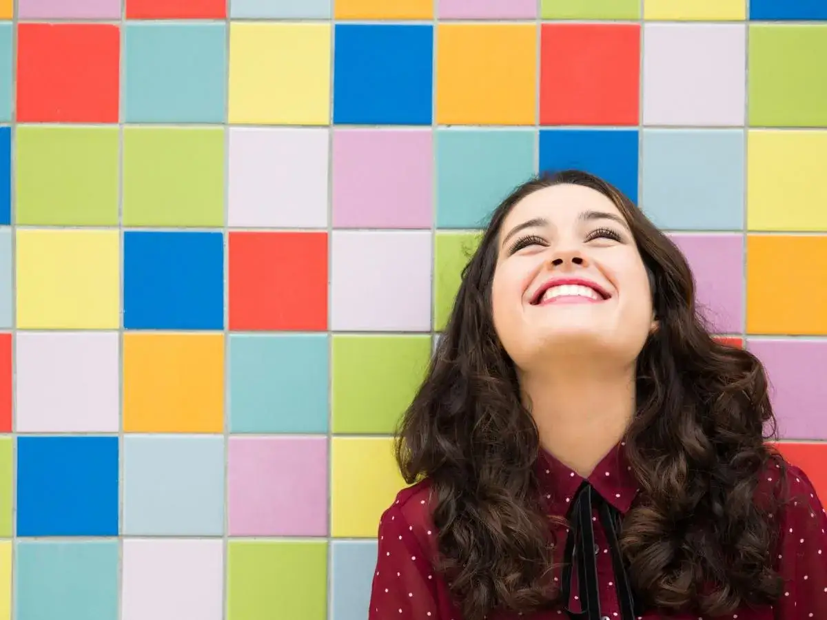 Ragazza sorridente guarda in alto, un esempio di come essere felici, su sfondo colorato a quadretti.