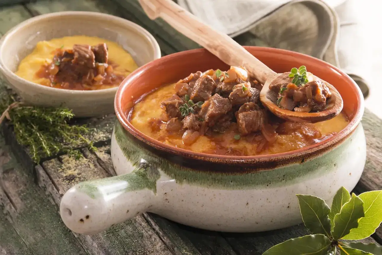 Un saporito gulash trentino servito su polenta cremosa, con un mestolo che ne raccoglie un boccone.