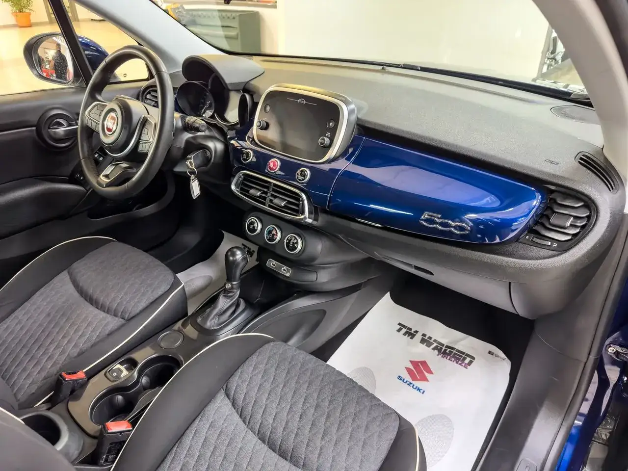 Interno di un'auto con cambio automatico. Sedili grigi con cuciture bianche, cruscotto blu lucido con logo 500.