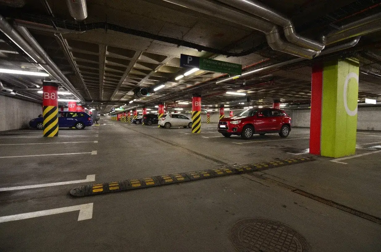 Wrocław Główny parking cennik: podziemny parking z czerwonym SUV-em, niebieskim autem i białym hatchbackiem.
