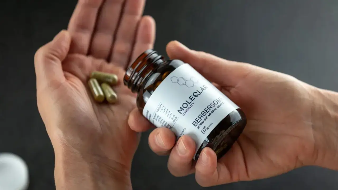 Mani che tengono capsule e un flacone di integratore. La berberina a cosa serve? Questo prodotto contiene berberina per il benessere.