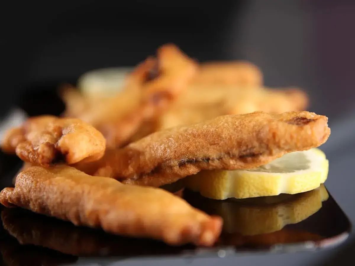 Délicieux beignets de sardines dorés et croustillants, servis avec des rondelles de citron sur une assiette noire.