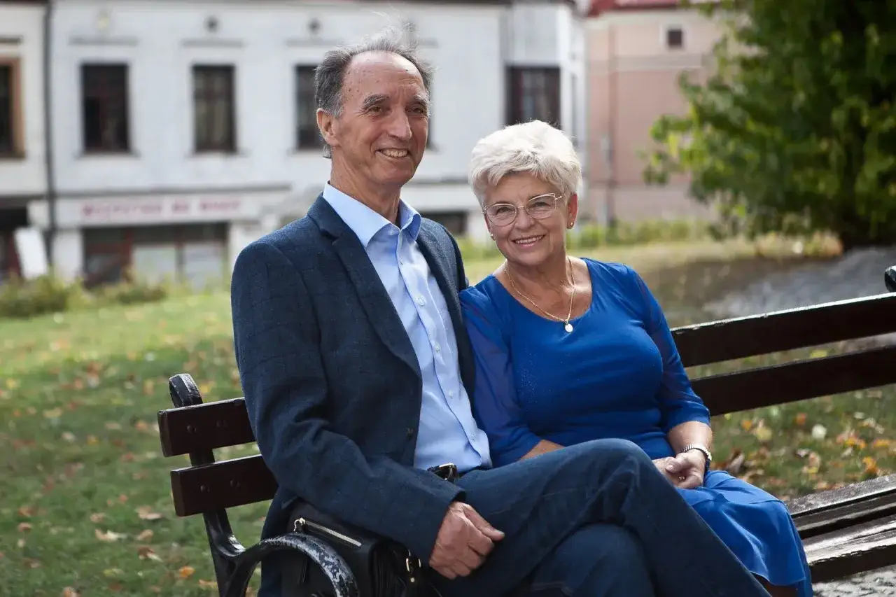 Uśmiechnięta para, facet po 50. i jego żona, siedzą na ławce w parku.