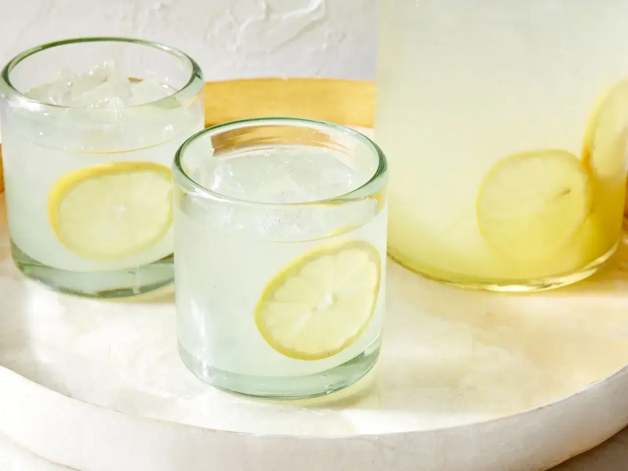 Erfrischendes Ingwer Wasser mit Zitronenscheiben in Gläsern und einer Karaffe, serviert auf einem Tablett.