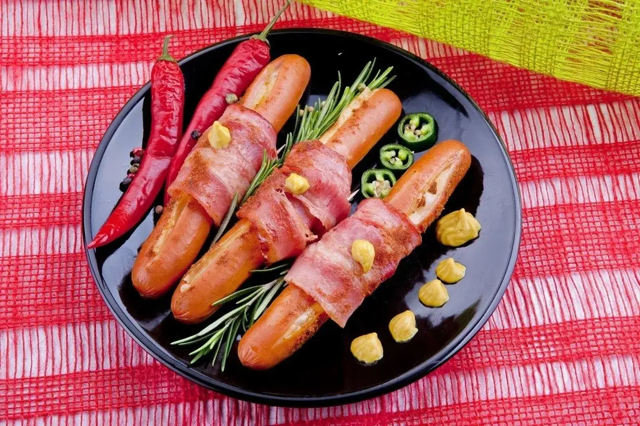 Parówki po kanadyjsku zawinięte w boczek, podane z musztardą, papryczkami chili i rozmarynem.