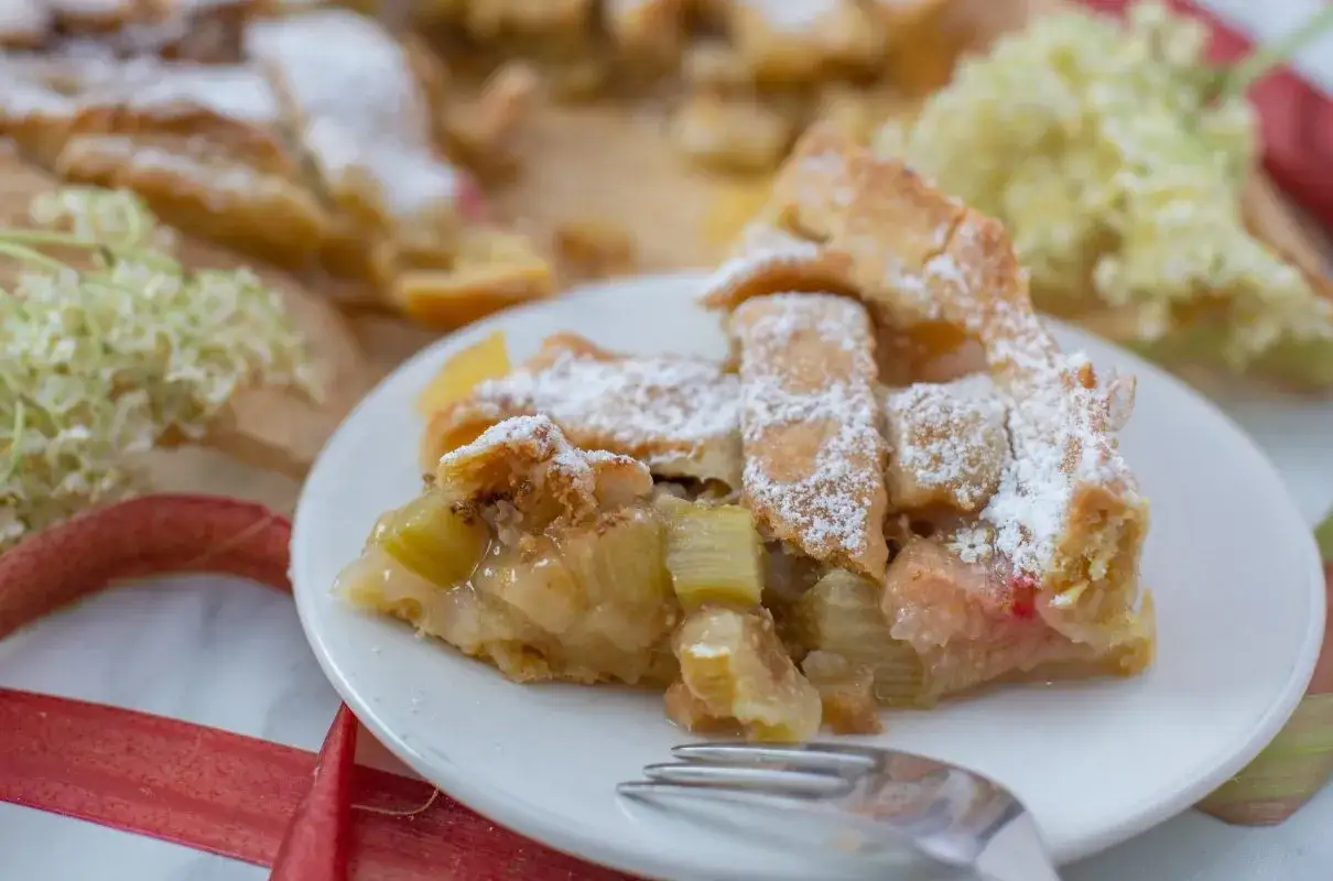 Pyszna tarta rabarbarowa z kruszonką, posypana cukrem pudrem, na talerzyku z widelcem.