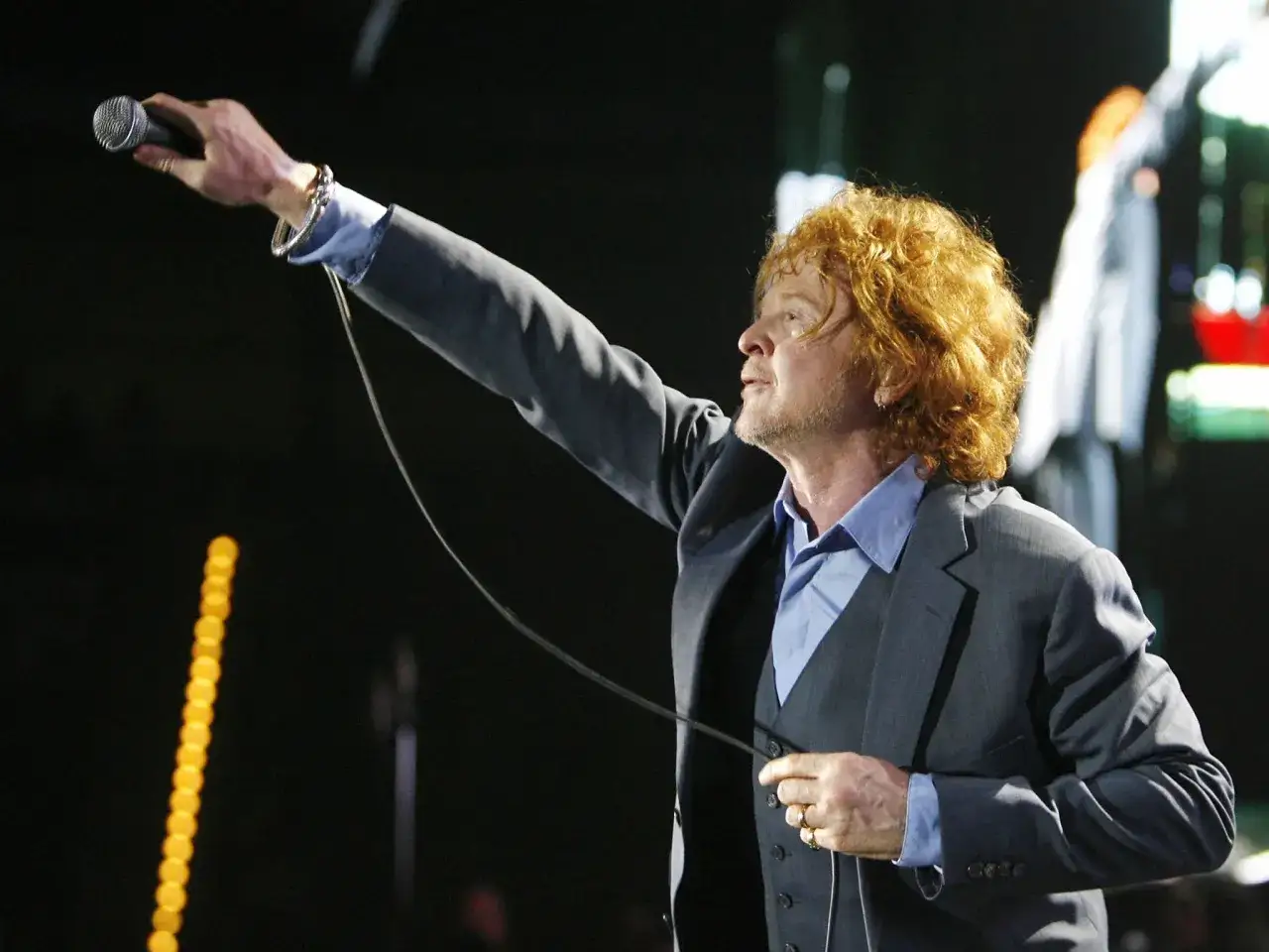 Wokalista Simply Red z rudymi włosami, w garniturze, śpiewa do mikrofonu na koncercie.
