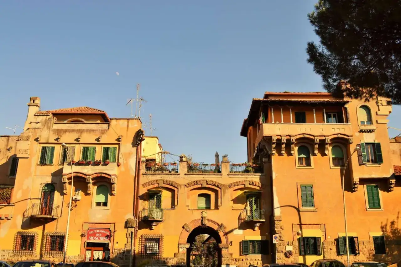 Edifici color ocra con balconi e persiane verdi, un arco in mattoni e un cartello 