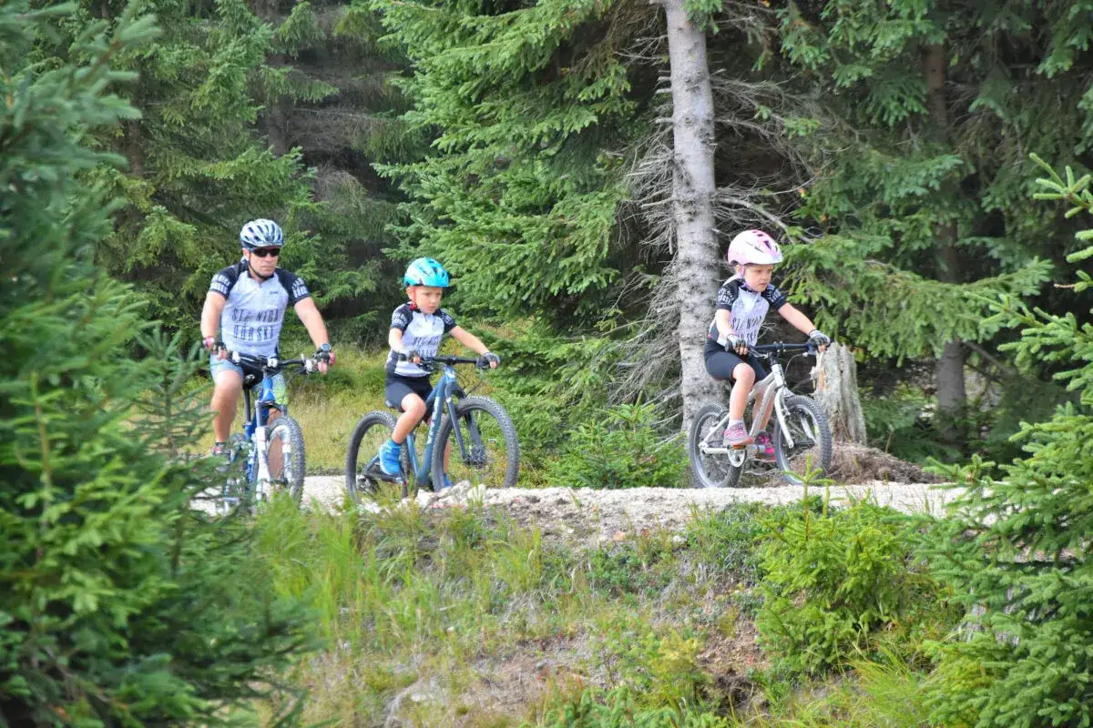 Rodzina na rowerach przemierza malownicze trasy rowerowe Szklarska Poręba. Dzieci z uśmiechem pokonują leśne ścieżki.