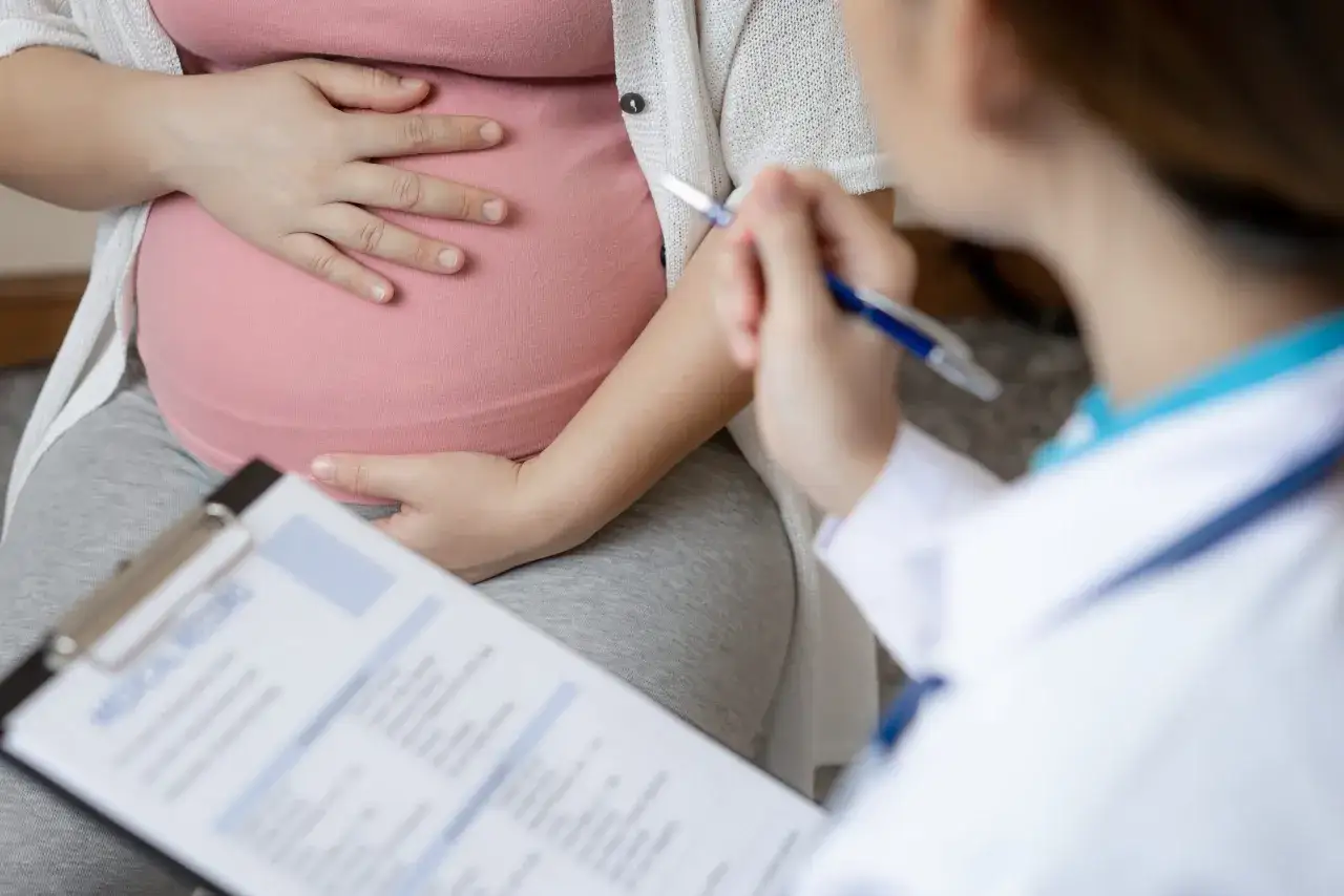 Lekarz rozmawia z ciężarną o tym, czy w menopauzie można zajść w ciążę. Kobieta trzyma dłoń na brzuchu.