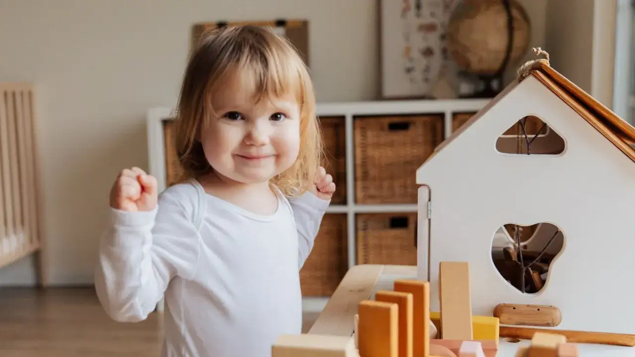 Niña sonriente jugando con bloques de madera, un ejemplo de la evolución del lenguaje en bebés.