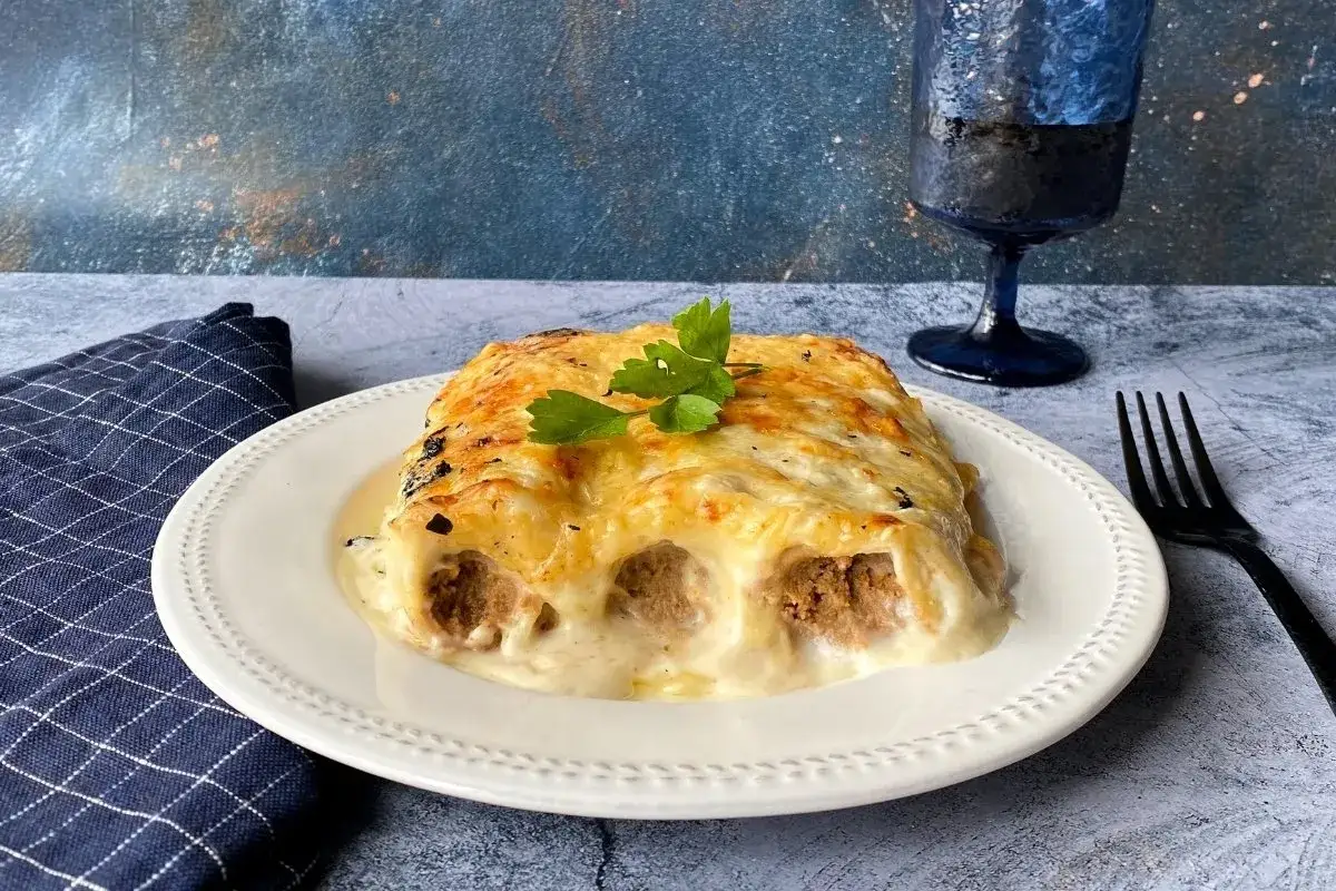 Canelones de carne gratinados, cubiertos con una cremosa bechamel y decorados con perejil fresco. Un plato reconfortante listo para disfrutar.