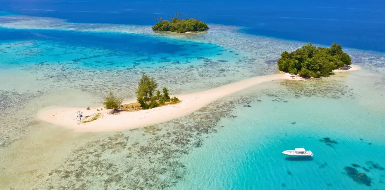 Bateau blanc naviguant dans les eaux turquoise des &icirc;les Salomon, pr&egrave;s d'&icirc;lots verdoyants et d'une langue de sable blanc.