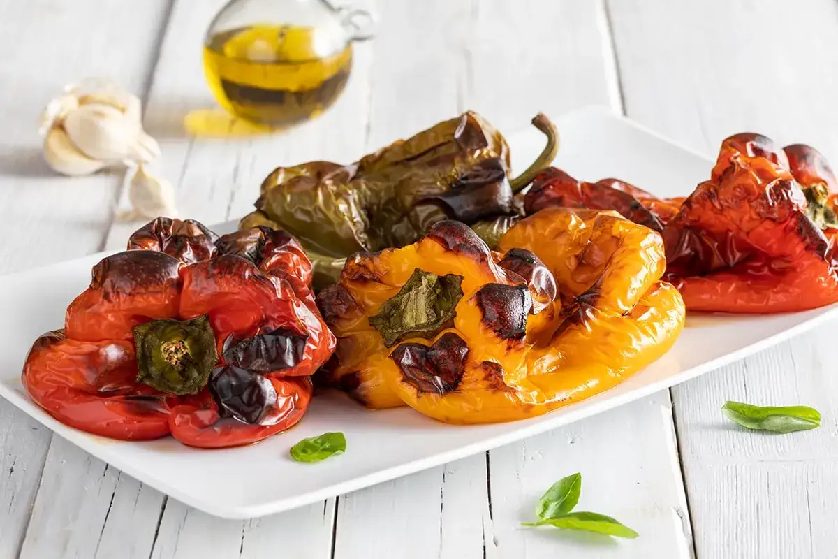 Un piatto di insalata di peperoni arrostiti, colorati e succosi, con aglio e olio d'oliva sullo sfondo.