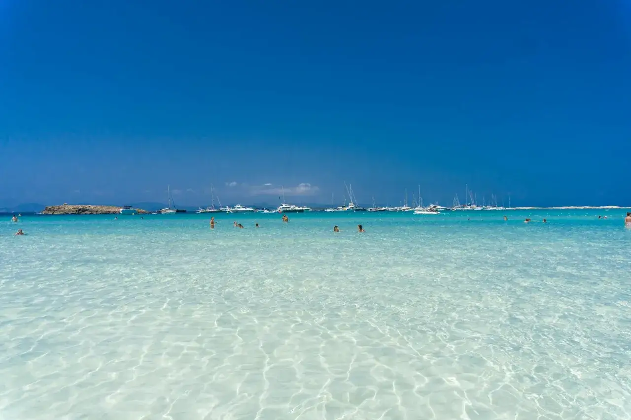 Aguas cristalinas y barcos anclados en un día soleado, un paraíso que confirma las **mejores playas de Formentera**.