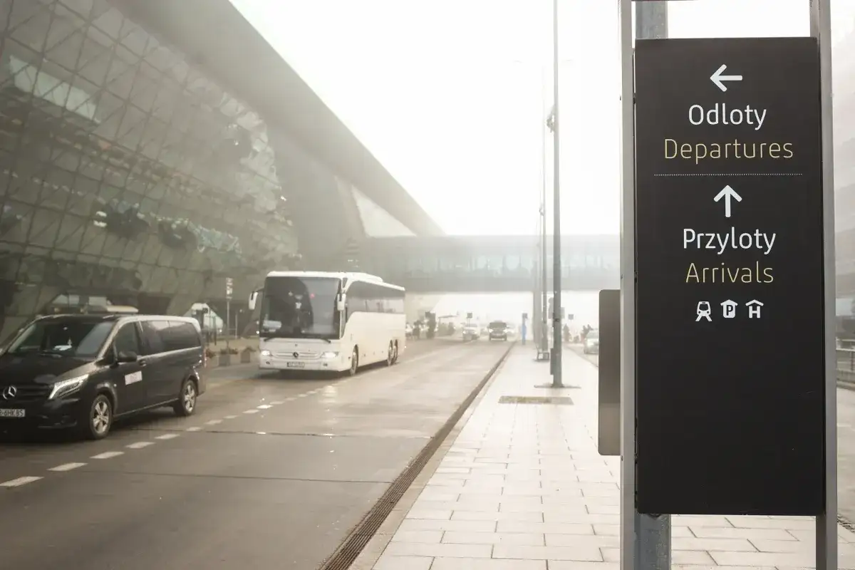 Znak kierujący na lotnisko Balice przyloty. Widać autobus i samochód osobowy.