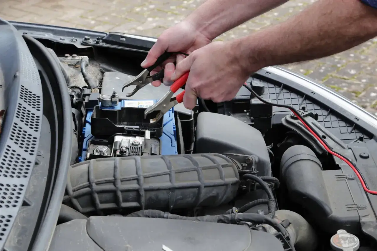 Ręce podłączają kable rozruchowe do akumulatora, bo auto nie odpala, mimo że akumulator jest sprawny.