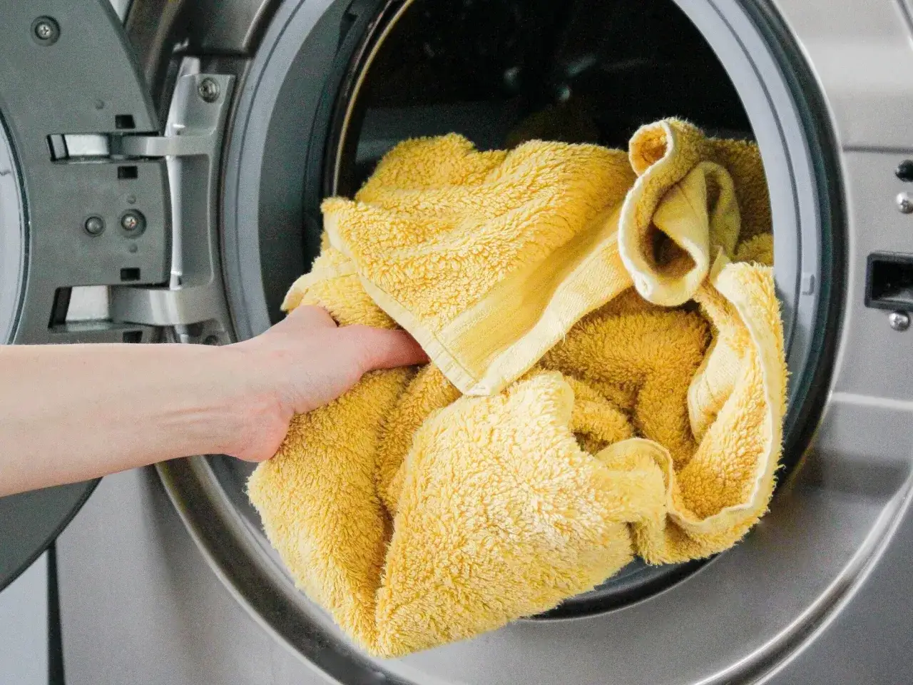 Eine Hand legt ein gelbes Handtuch in eine Waschmaschine. So einfach ist es, zu lernen, wie man eine Waschmaschine benutzt.