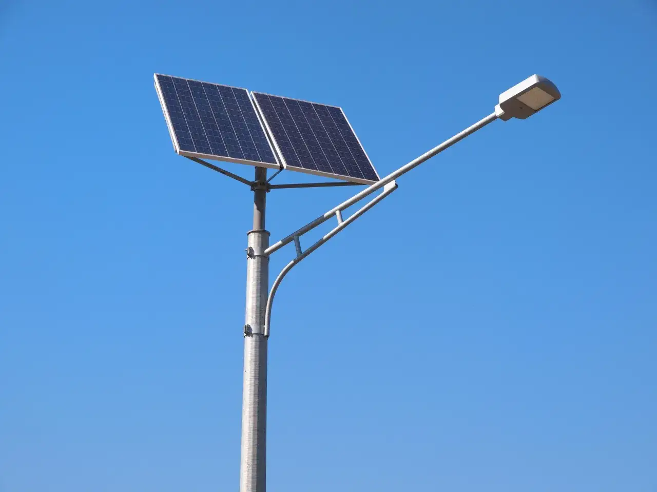 Słup z dwoma panelami słonecznymi i lampą LED, idealny jako lampy na taras solarne, na tle błękitnego nieba.