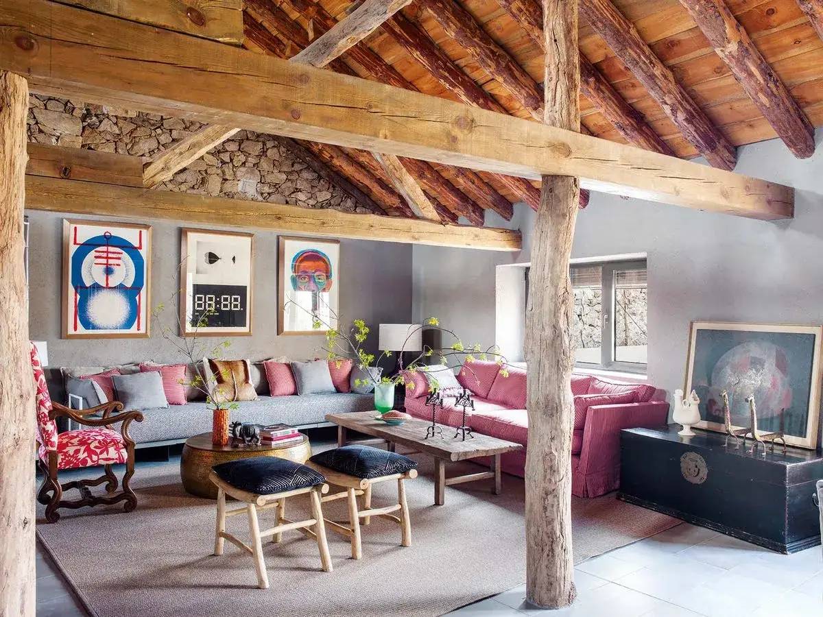 Salón rústico con vigas de madera, sofás coloridos y arte moderno. Un ejemplo de casas con encanto que combinan lo tradicional y lo contemporáneo.
