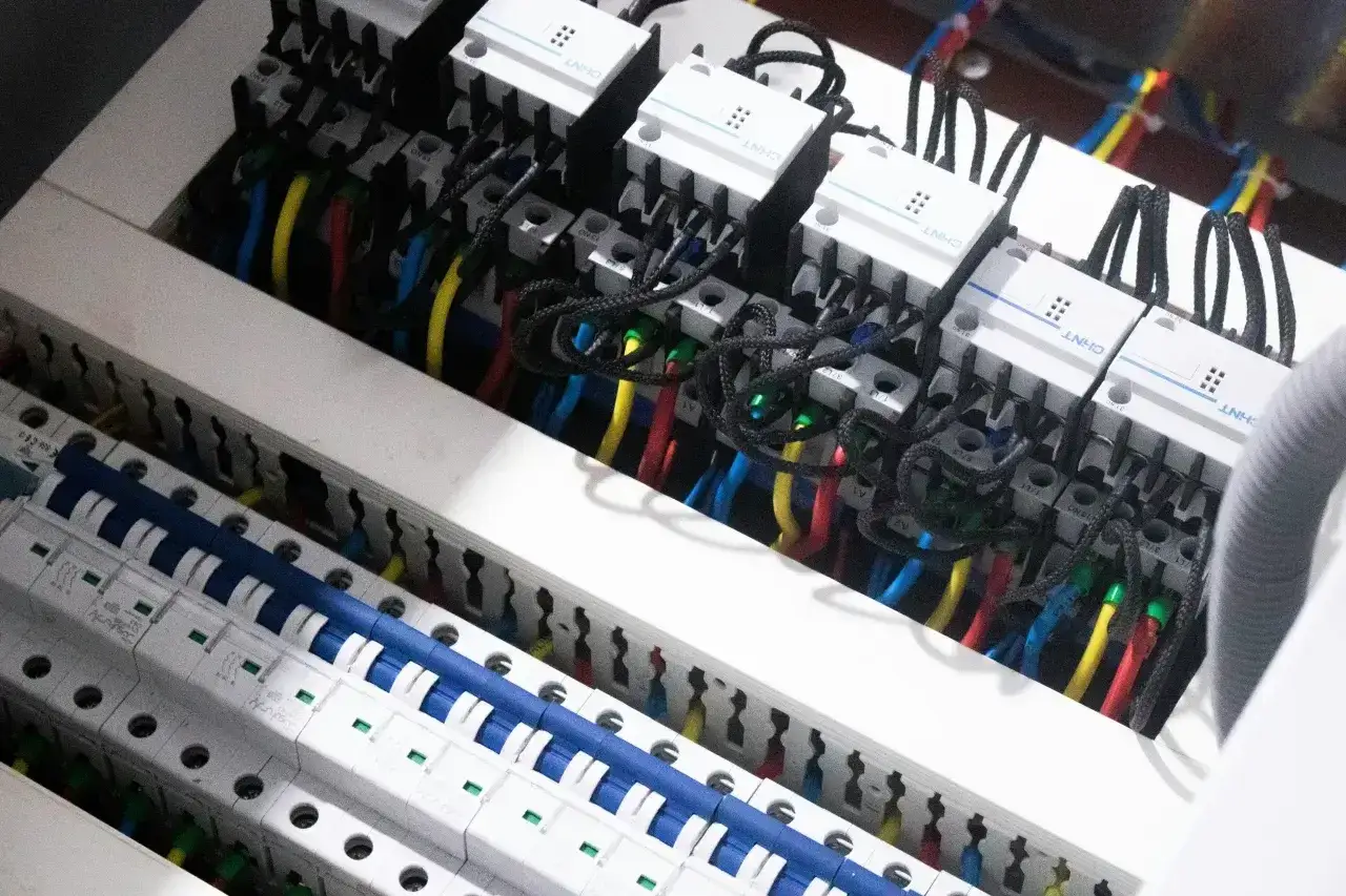 Wnętrze skrzynki elektrycznej z przewodami i wyłącznikami. Widać moduły z oznaczeniami, które kontrolują przepływ prądu, jednostka natężenia prądu.