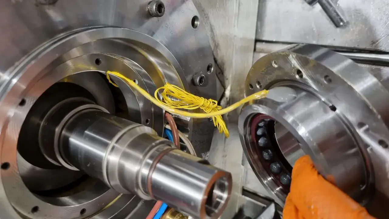 Metalowe części do frezarki, w tym wałek i łożysko z kulkami. Żółte przewody oplatają mechanizm.