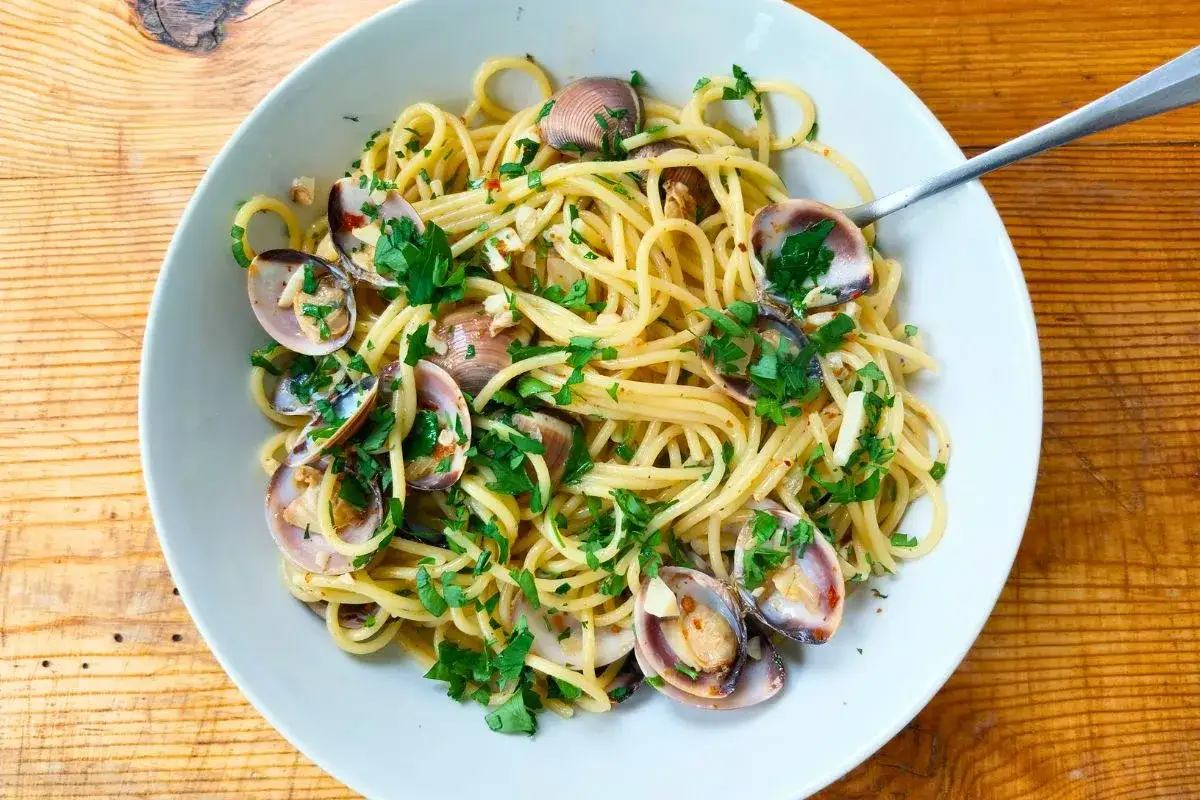 Spaghetti Vongole, ein Klassiker der italienischen K&uuml;che, mit frischer Petersilie und Muscheln, serviert in einer wei&szlig;en Sch&uuml;ssel auf Holzhintergrund.