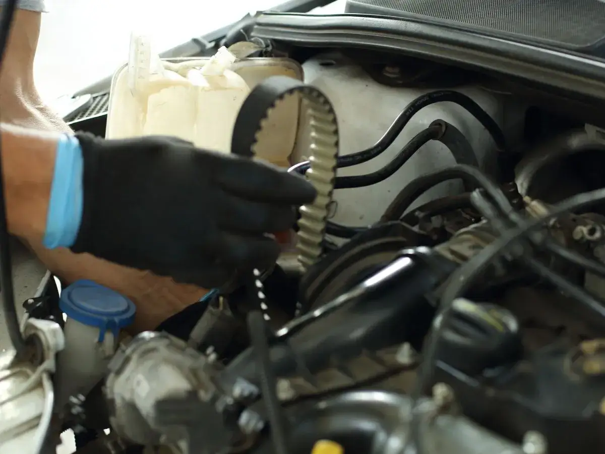 Mechanik w czarnej rękawicy trzyma pasek rozrządu. Czas na wymianę, bo rozrząd co ile km to ważna sprawa dla silnika.