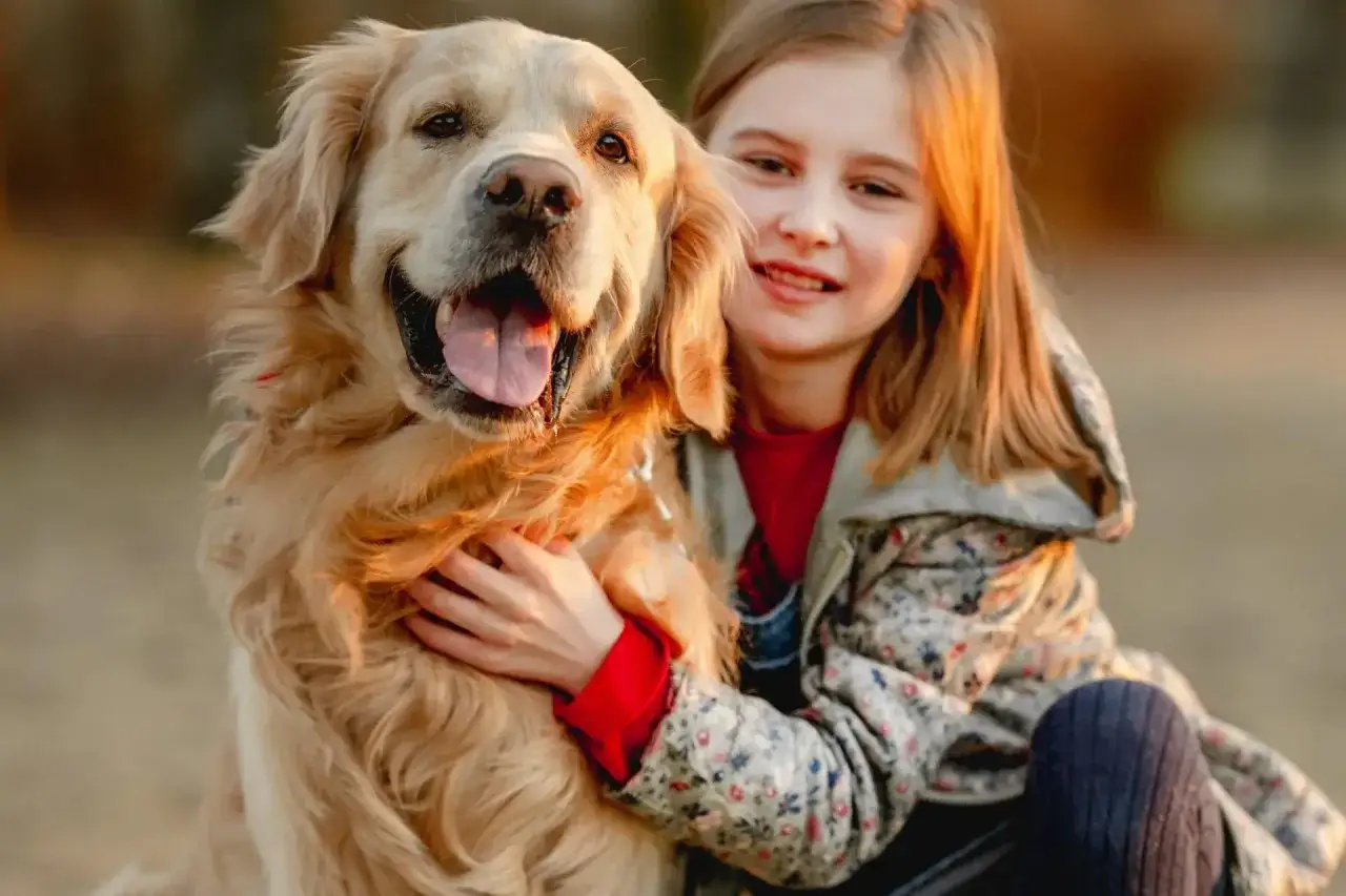 Uśmiechnięta dziewczynka tuli swojego wesołego golden retrievera.