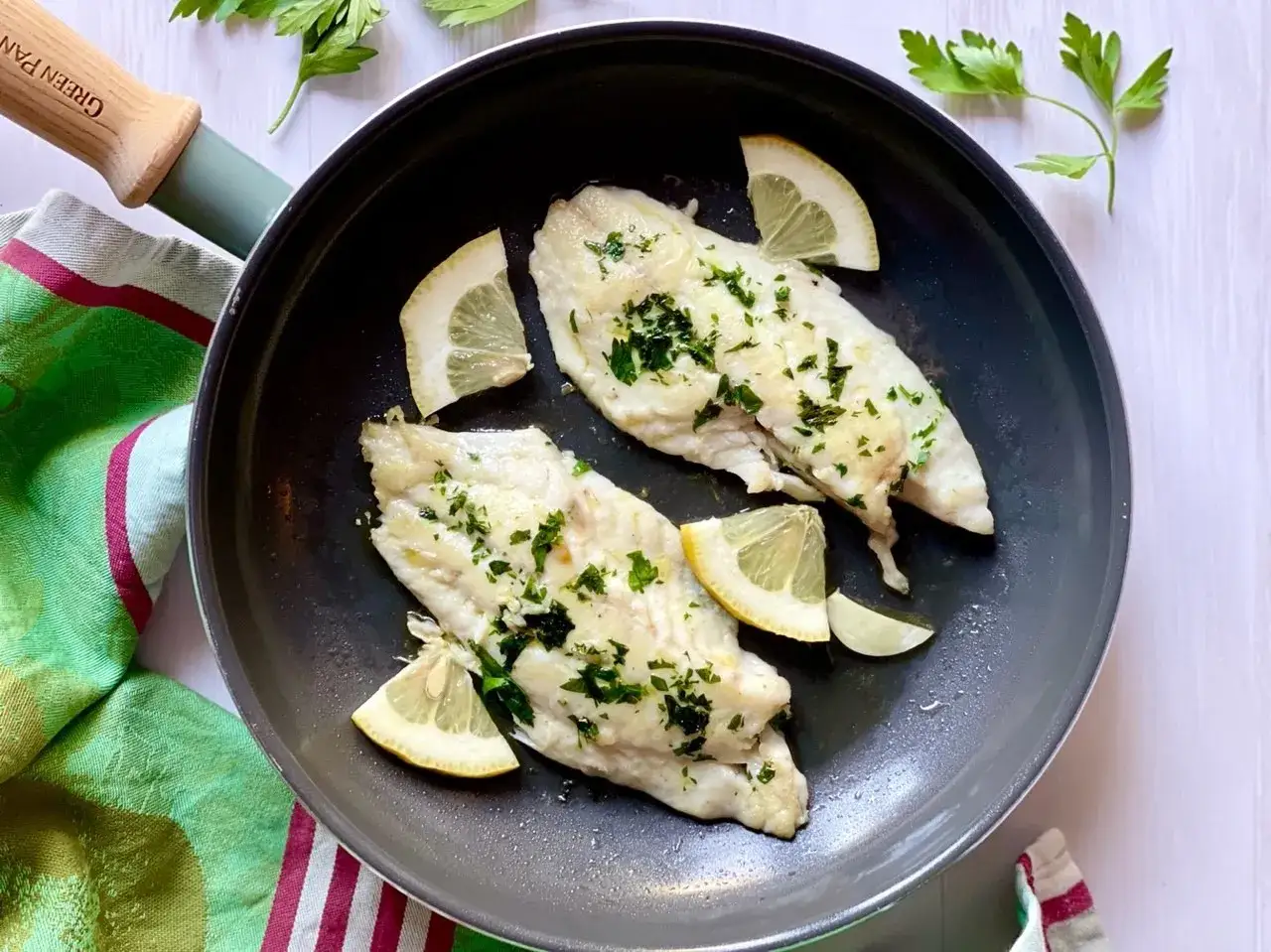 Orata in padella, cotta alla perfezione con limone e prezzemolo fresco, pronta per essere gustata.