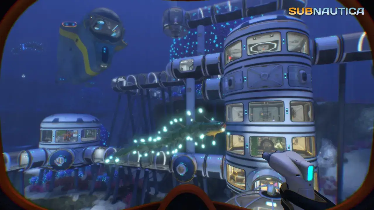 Vue d'une base sous-marine dans Subnautica. Un cyclope et un ver des profondeurs bioluminescent nagent près de la structure.