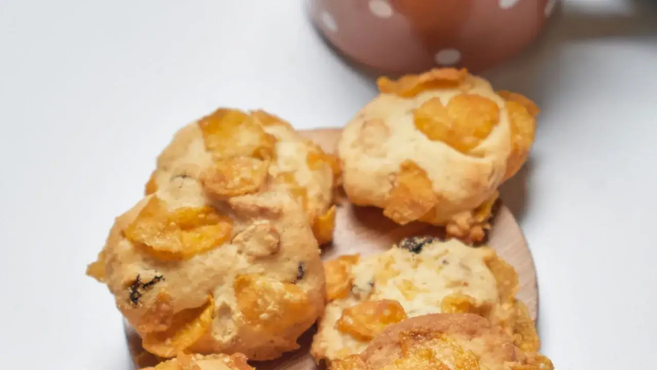 Biscotti croccanti con fiocchi di mais e uvetta, simili a rose del deserto, su un piatto di legno.