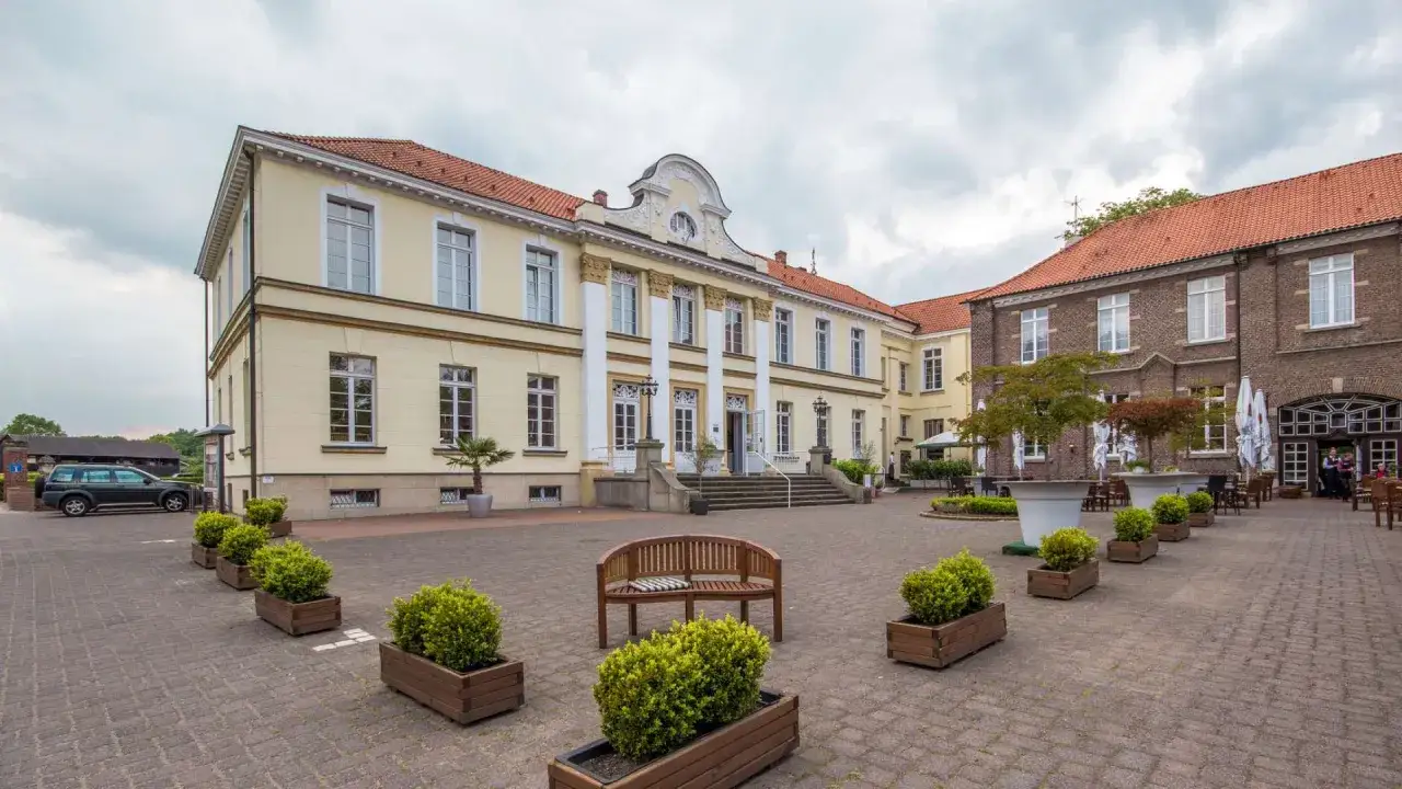 Das Schloss Westerholt, ein gelbes Herrenhaus mit Säulen, und ein Backsteingebäude mit Außensitzplätzen.