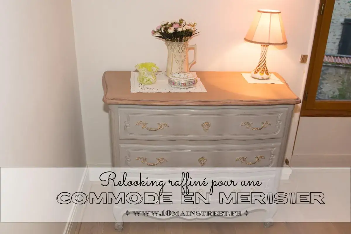 Commode en merisier modernisée, repeinte en gris doux avec des détails dorés. Un vase fleuri et une lampe complètent la scène.
