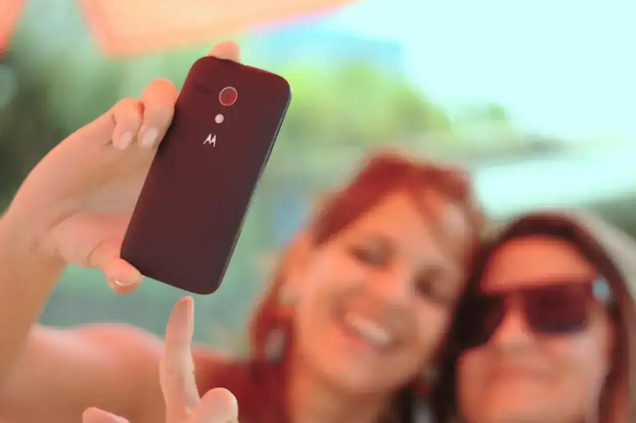 Dwie uśmiechnięte kobiety robią sobie selfie telefonem Motorola na tle zieleni.