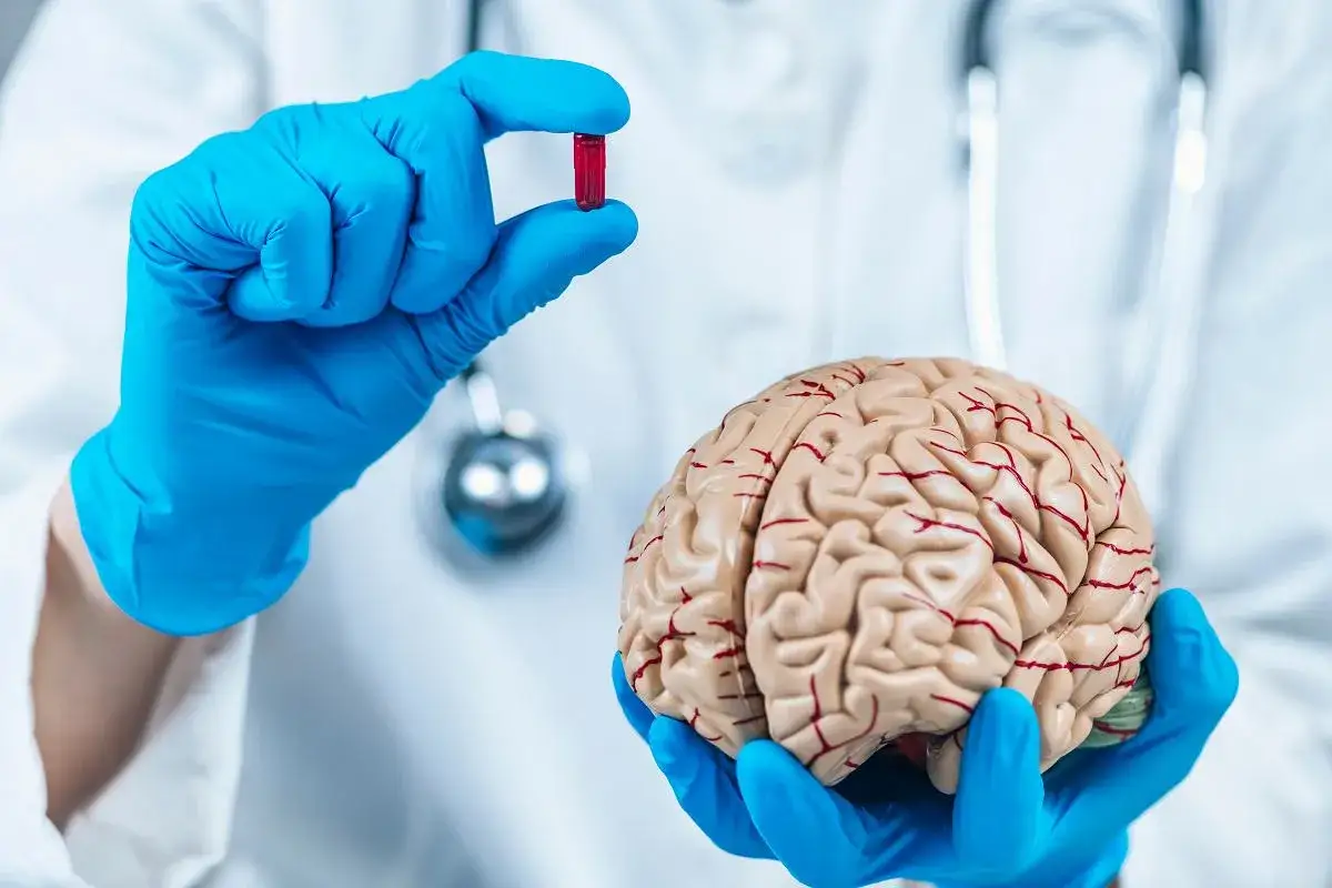Lekarz w niebieskich rękawiczkach trzyma kapsułkę i model mózgu, symbolizując, co to znaczy placebo.